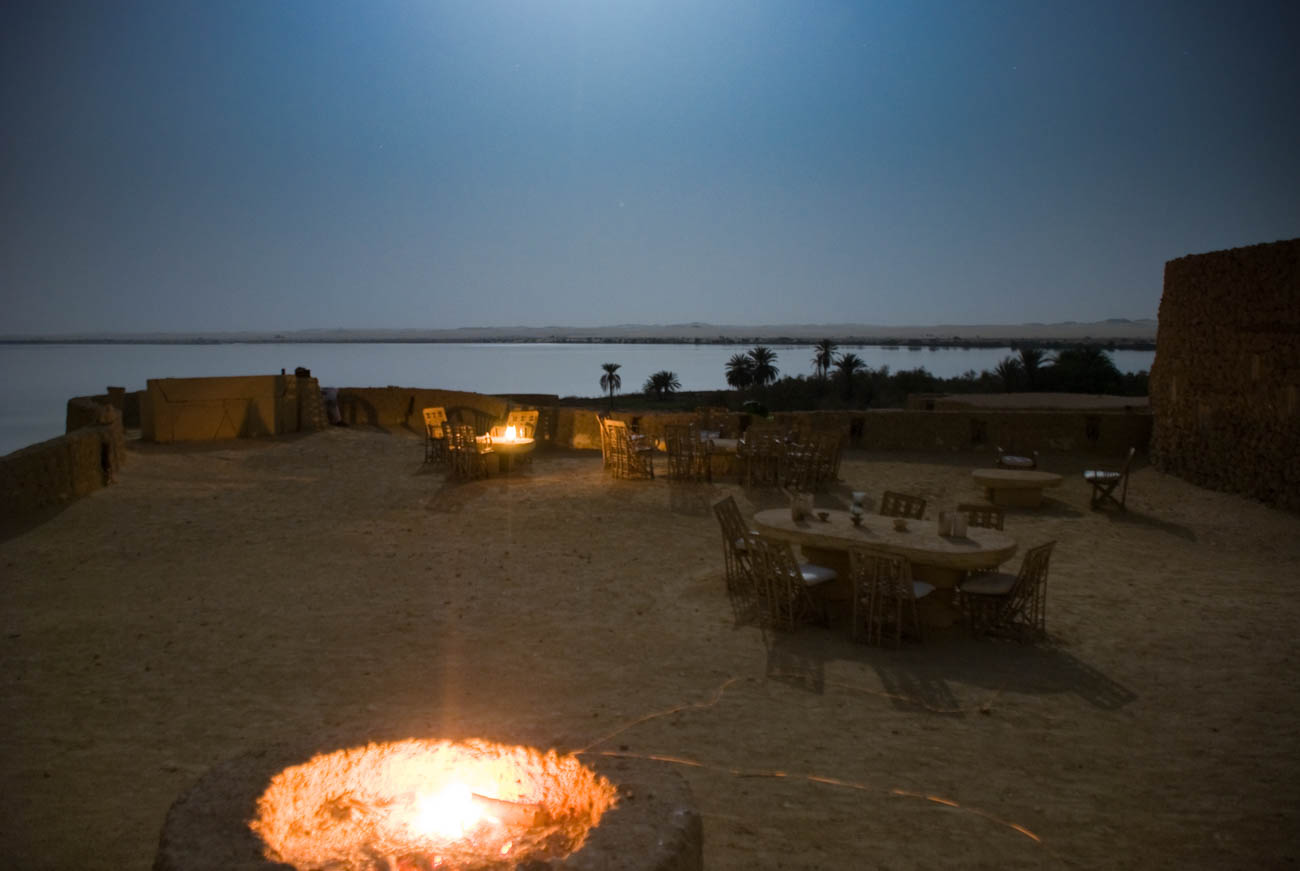 Traditional stone-built hotel in Siwa Oasis surrounded by palm trees and desert landscape.