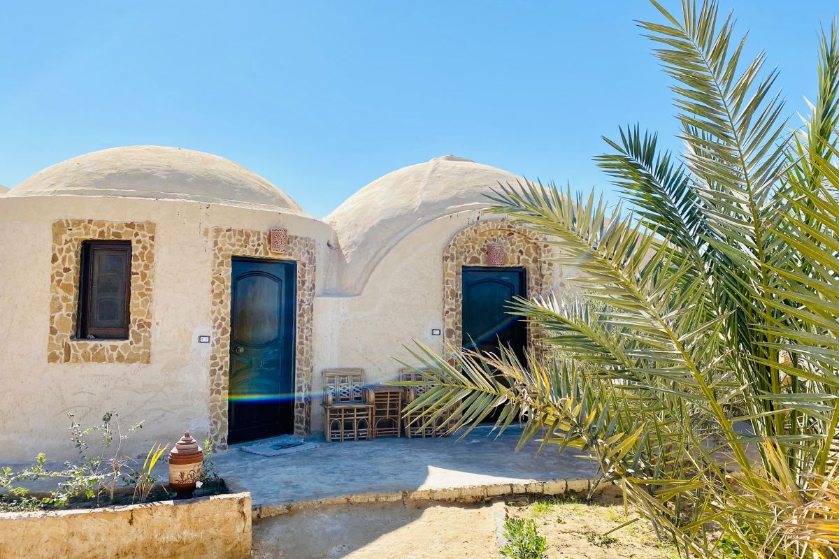 Panoramic view of a serene desert landscape with traditional mud-brick structures and palm trees under a clear sky