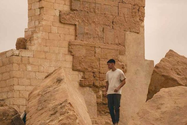 A man walks among the ancient stone ruins of Amun Temple, with crumbling walls and boulders surrounding the site.