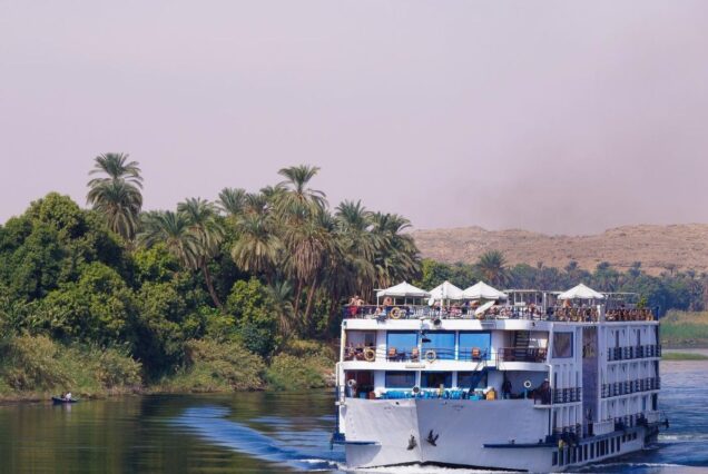 Felucca sailboat on the Nile River with a scenic view of palm trees and mountains in the background