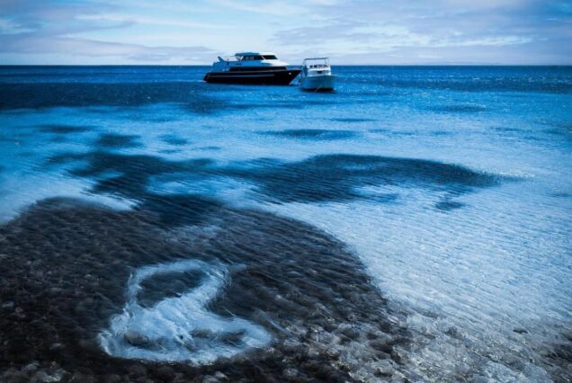 Two boats anchored over clear, shallow water with a visible coral reef below