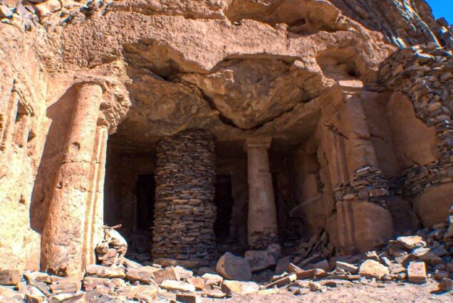 Ancient rock-carved structure with stone pillars and rocky surroundings under a blue sky