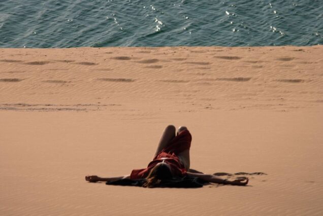 Woman lying on golden sand near the edge of a desert meeting the sea