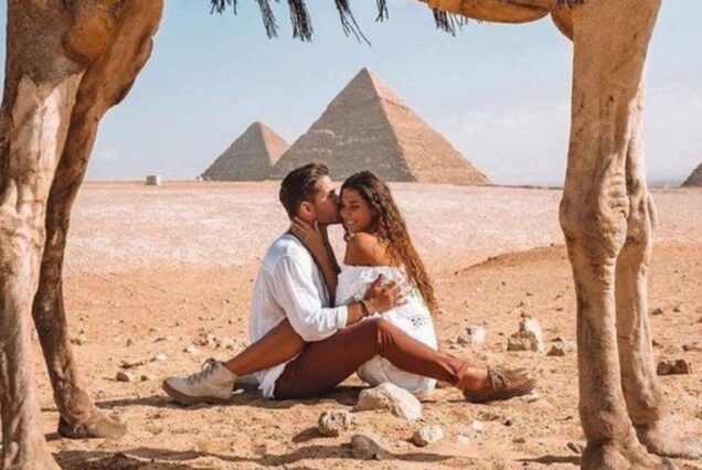 Romantic couple sitting near the Pyramids of Giza, framed by a camel's legs