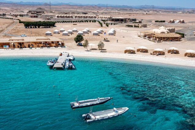 Aerial view of a desert beach resort with a pier and boats on clear turquoise water