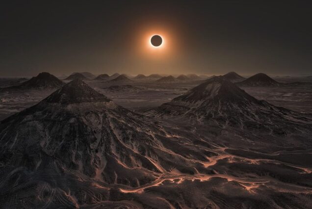 Solar eclipse over rugged mountain peaks in a vast desert landscape