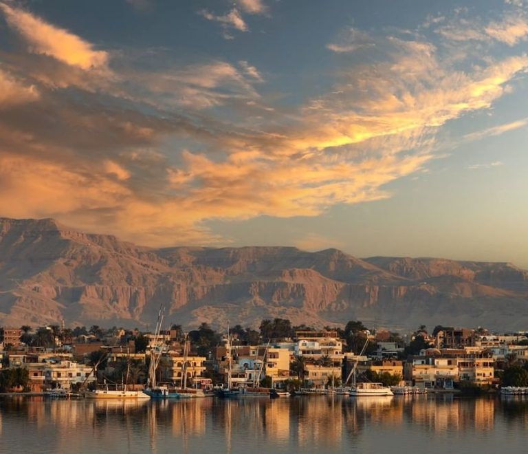 Luxor at sunset with boats on the Nile and mountains in the background