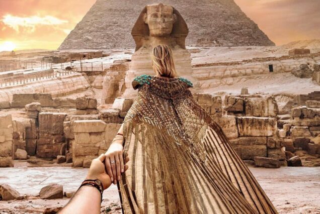 A woman in an elaborate gold cloak standing in front of the Great Sphinx with a pyramid in the background