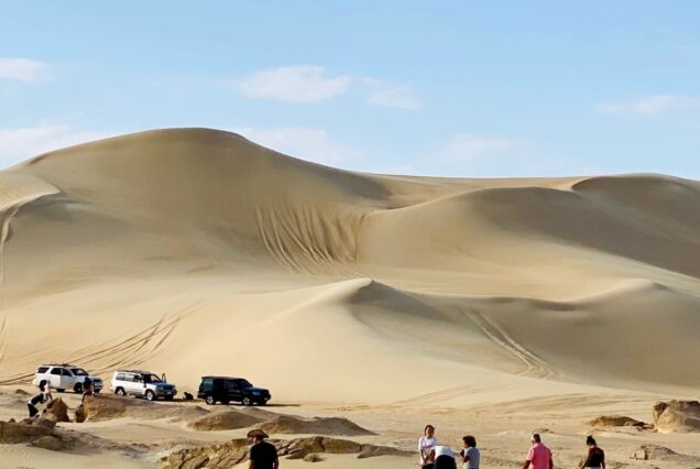 Four-wheel-drive vehicles in a vast desert with towering sand dunes