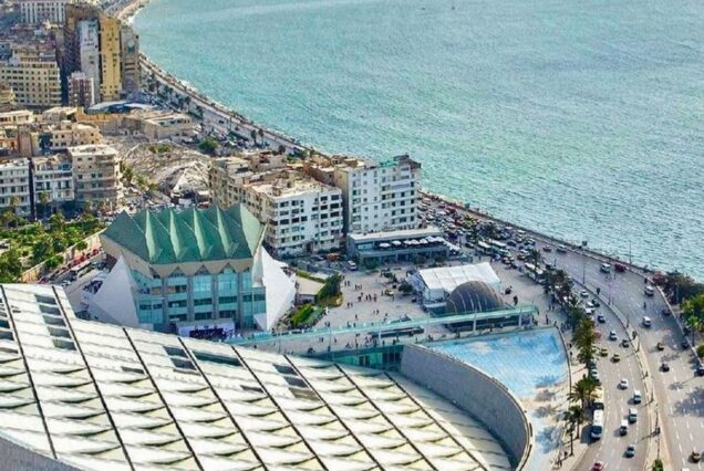 An aerial view of a coastal city with modern architecture and a long beachfront road along the sea