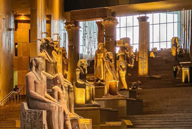 A museum hall with ancient Egyptian statues and columns, dimly lit with a warm golden glow