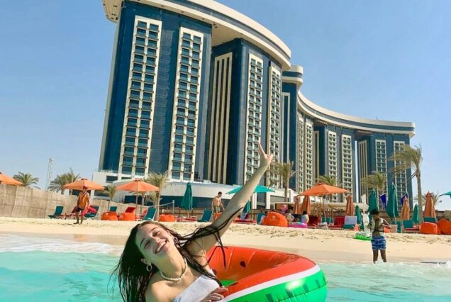 A woman floating with an inflatable tube in front of a luxury hotel by the beach