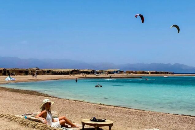 Woman sitting on a beach by the turquoise waters, with kite surfers in the background in Egypt