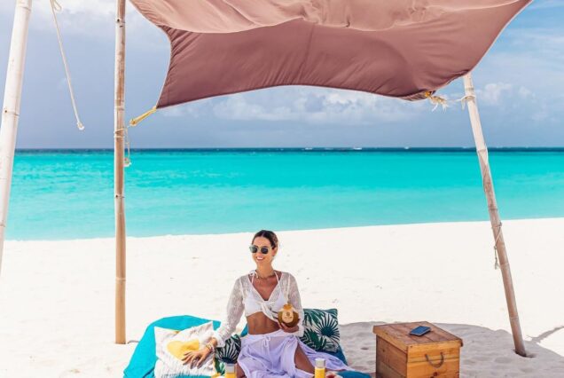 A woman relaxing under a sunshade on a tropical beach with turquoise waters in the background