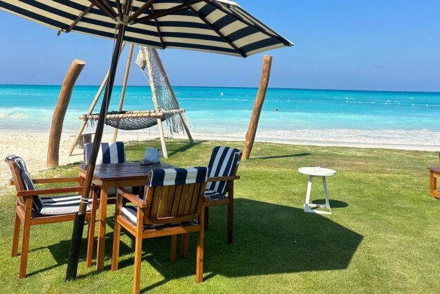 A relaxing beachside setup with a table, chairs, and an umbrella overlooking the turquoise ocean