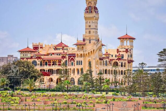 A majestic palace with red and yellow colors, surrounded by lush gardens and trees