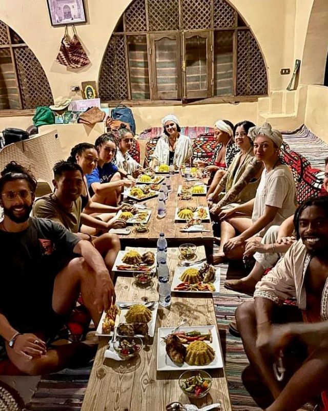 A group of friends and family sitting around a low dining table, enjoying a shared meal of traditional dishes in a cozy, rustic interior