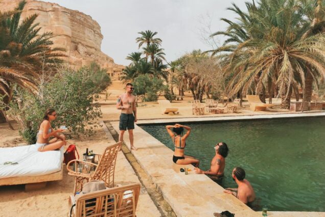 Tourists relaxing by a natural spring pool in the Egyptian desert surrounded by palm trees