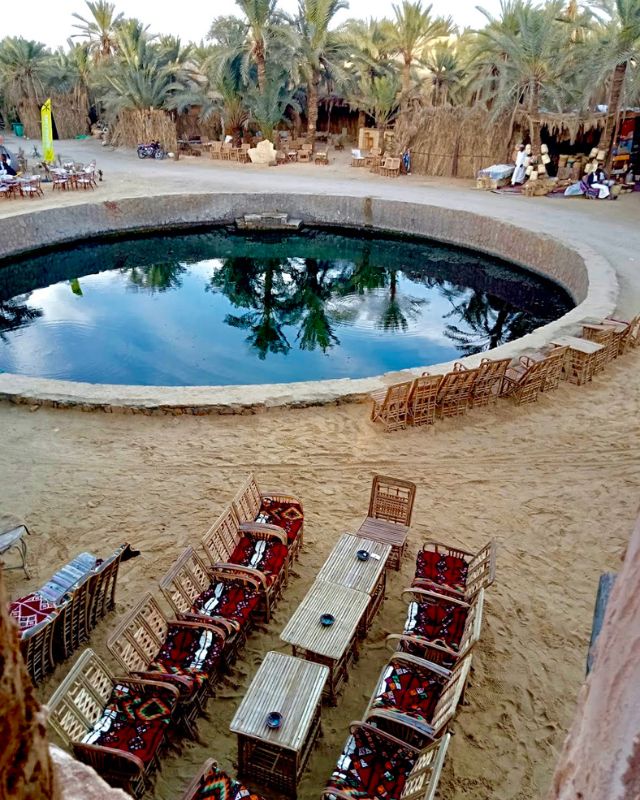 Traditional seating setup around a large circular pool, with wooden chairs and palm trees in the background
