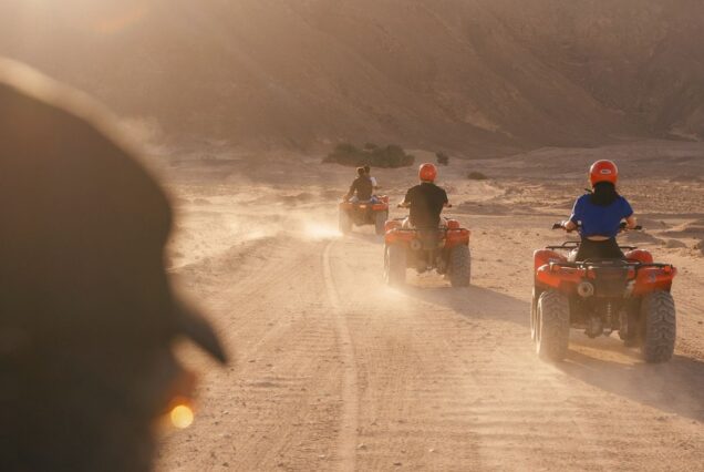 Group of people riding quad bikes through the desert at sunset