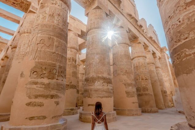 Woman in a white dress standing among towering hieroglyph-covered columns in an ancient Egyptian temple
