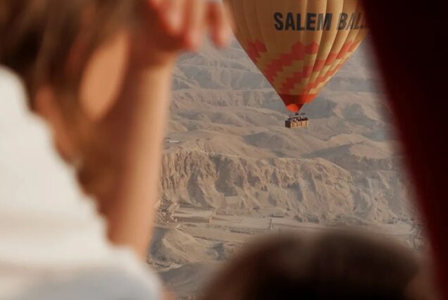 A hot air balloon floating over the ancient ruins and desert landscape of Luxor, Egypt