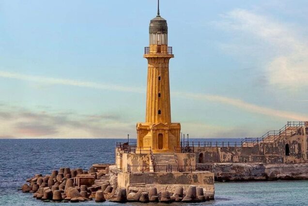 A yellow lighthouse on a rocky shore, overlooking the calm blue sea