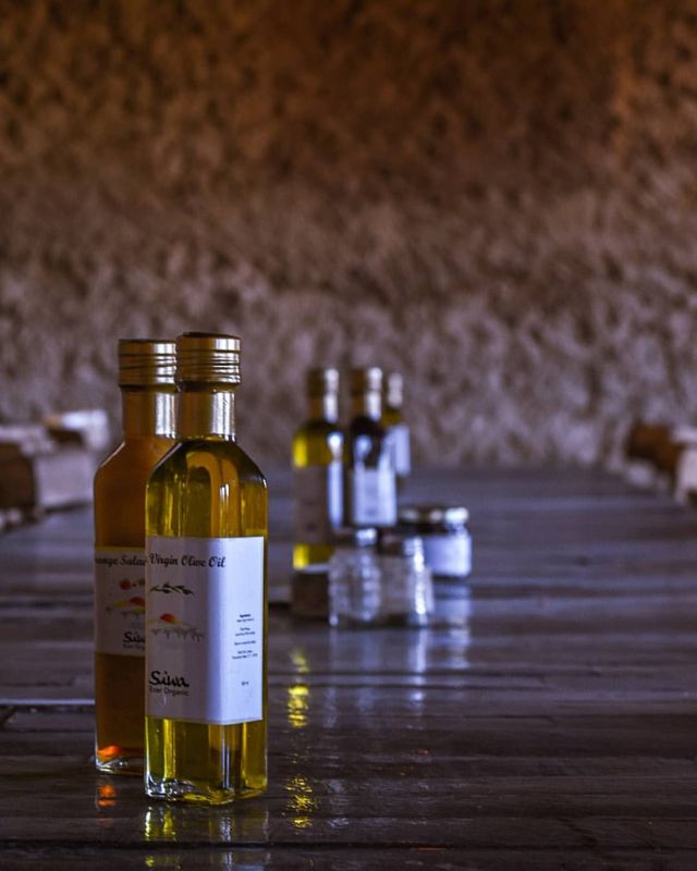 long wooden dining table lined with olive oil bottles and jars, set against a rustic, earthen wall