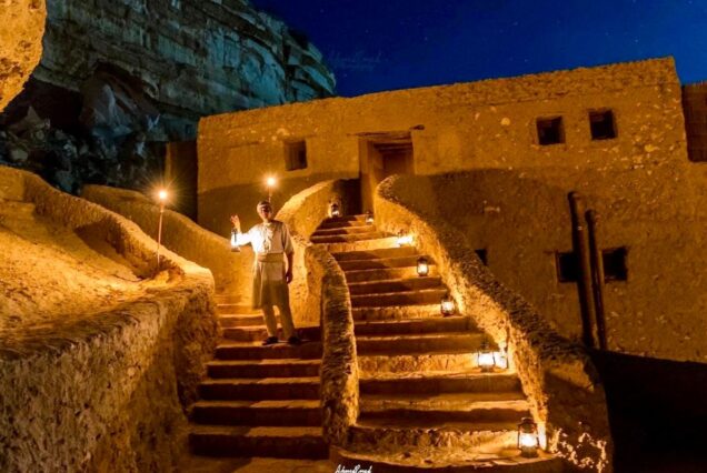 A man holding a lantern standing on historic stone stairs at night in Egypt