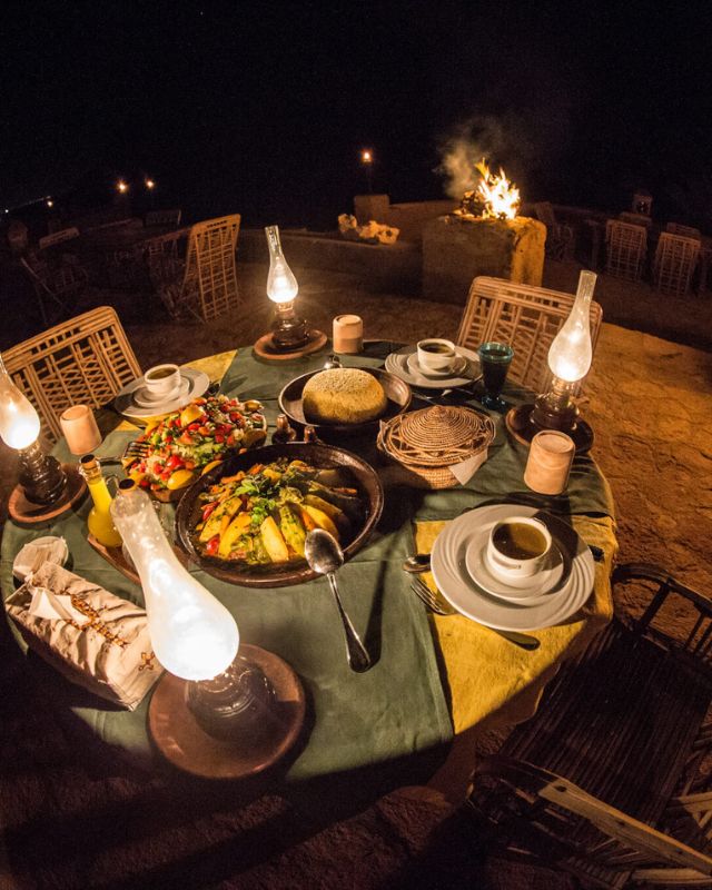 A dinner table set with traditional dishes and lamps under the night sky.