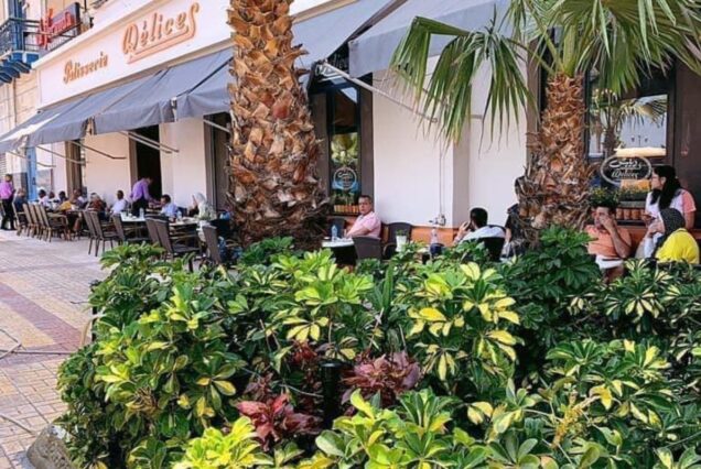 Patrons enjoying outdoor seating at a café surrounded by greenery and palm trees