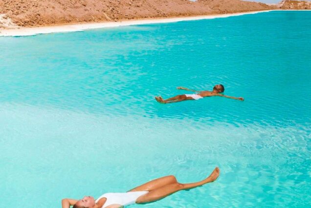 People floating in the turquoise waters of a salt lake surrounded by desert in Siwa Oasis