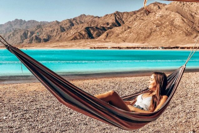 Woman relaxing in a hammock by a turquoise lagoon with desert mountains in the background