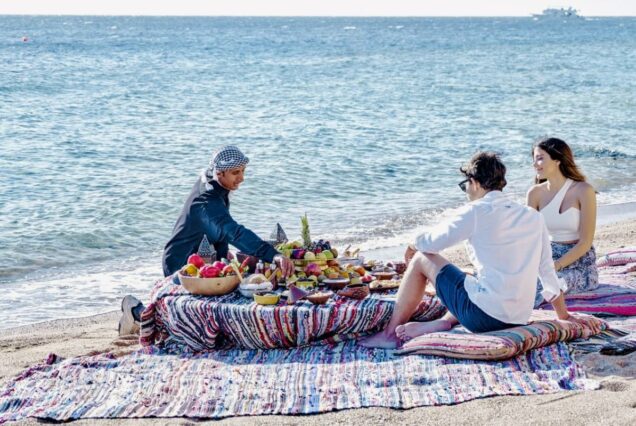 Couple enjoying a private picnic by the beach set up with colorful cushions and traditional decor