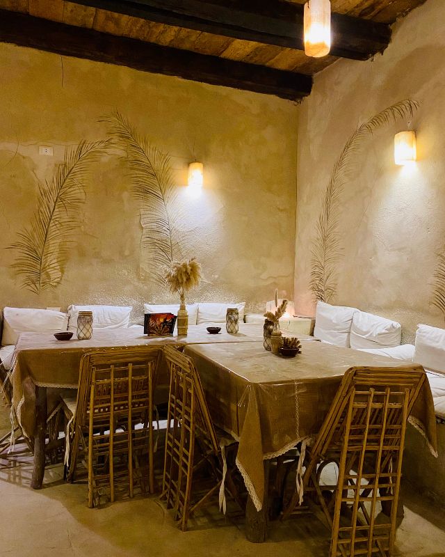 An inviting indoor dining space with natural woven chairs, a rustic table, and soft lighting in a desert-inspired room