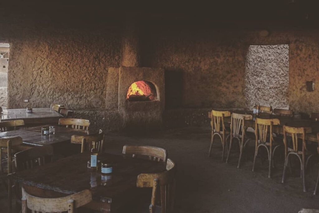 A cozy, dimly lit restaurant with wooden tables and a traditional wood-fired oven in the background, casting a warm glow