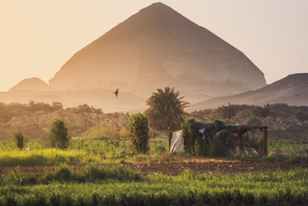 Sunset view of a pyramid with greenery and a small shelter in the foreground