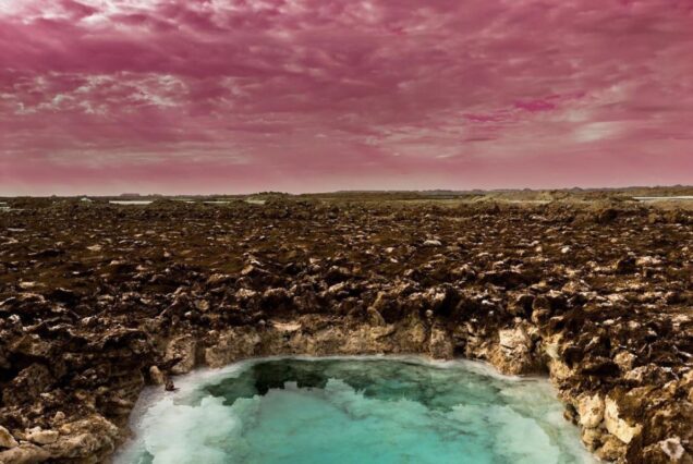 A salt pool in the desert with a vivid pink sky overhead, creating a surreal and dreamlike atmosphere