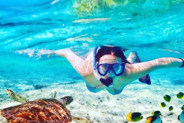 Woman snorkeling underwater near a sea turtle and colorful fish