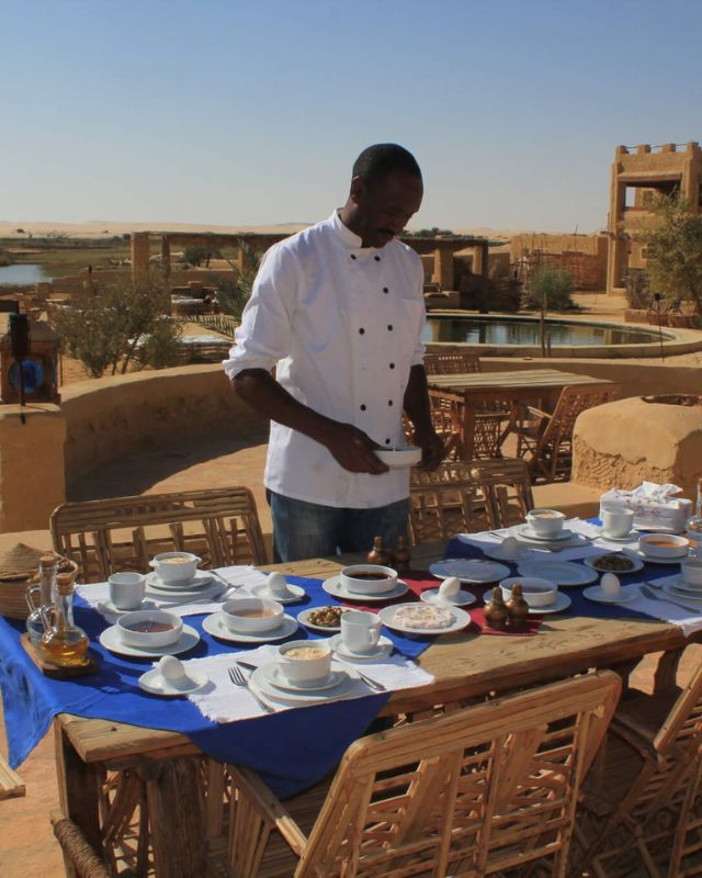 A chef setting a table with a variety of dishes for breakfast outside in a desert resort