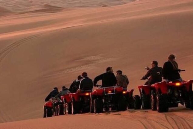 Group of people riding quad bikes through the sand dunes at sunset in the Egyptian desert