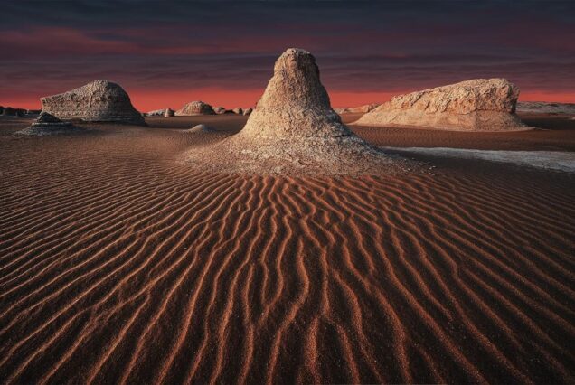 Unique rock formations in a desert at sunset with rippled sand patterns