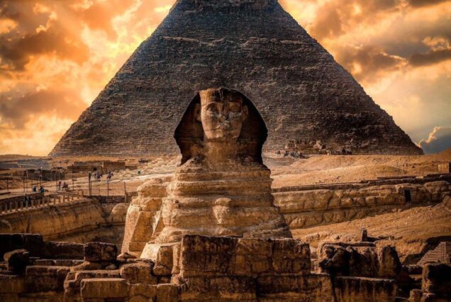 The Great Sphinx with the Pyramid of Giza in the background, under a dramatic sky