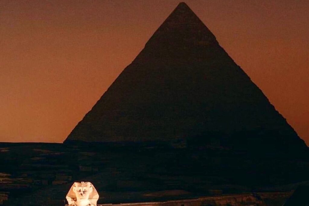 The Sphinx illuminated with the Great Pyramid silhouetted against a dusky sky