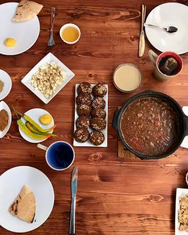 An overhead view of a traditional meal spread, featuring plates of bread, spices, a stew in a cast-iron pot, and other local dishes on a wooden table