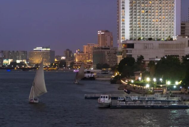 River with traditional sailboats and modern buildings in the background at dusk