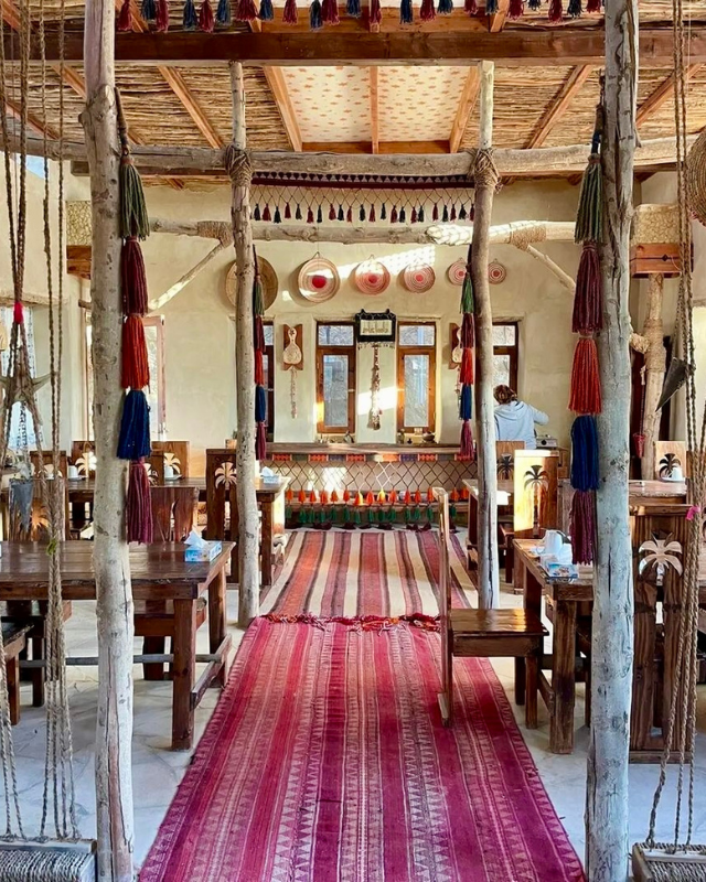 An eclectic dining area decorated with colorful tassels, rustic wooden furniture, and traditional textiles. A red patterned carpet runs through the center of the room