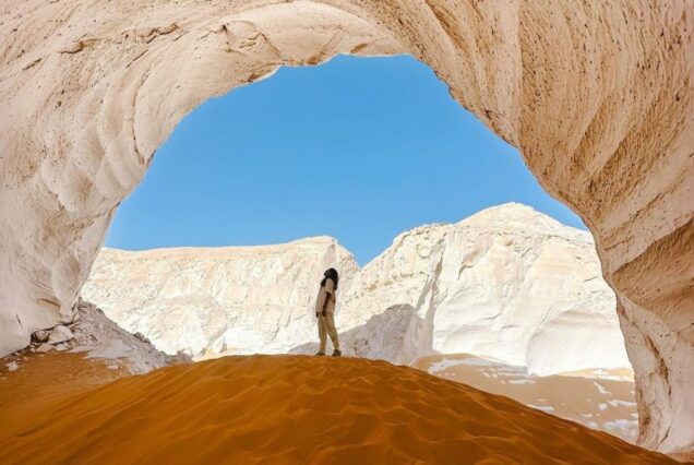 Person standing under a natural rock arch in a desert landscape