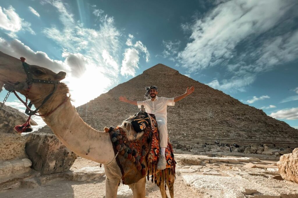 Man riding a camel near the Great Pyramid with arms outstretched