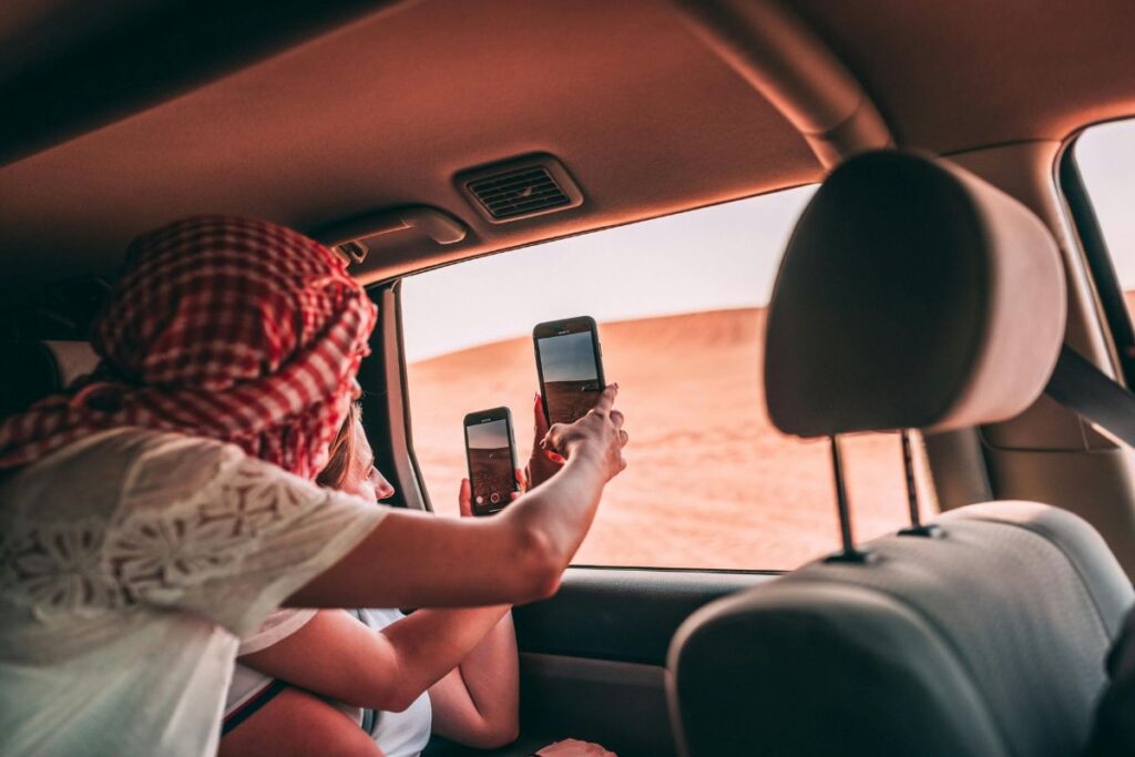 Two people taking photos of the desert landscape from inside a car